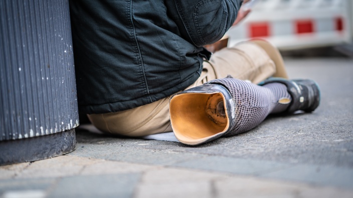 Auf diesem Bild sehen Sie eine auf dem Boden sitzende, obdachlose Person.