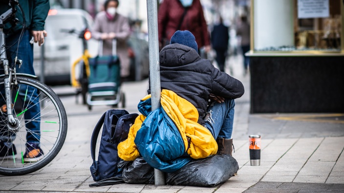 Auf diesem Bild sehen Sie einen auf dem Boden sitzenden, obdachlosen Menschen.